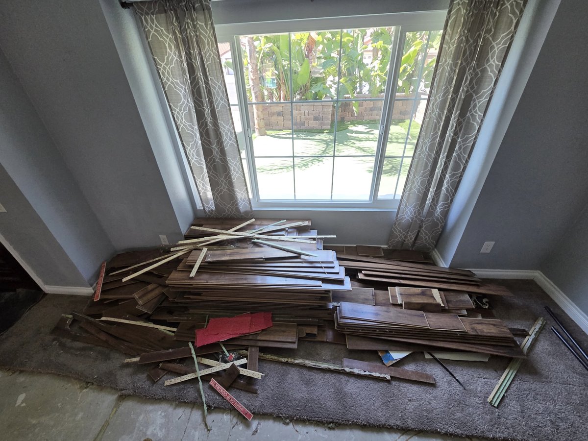 Living room with ripped-up hardwood planks and tack strips piled under the window, before