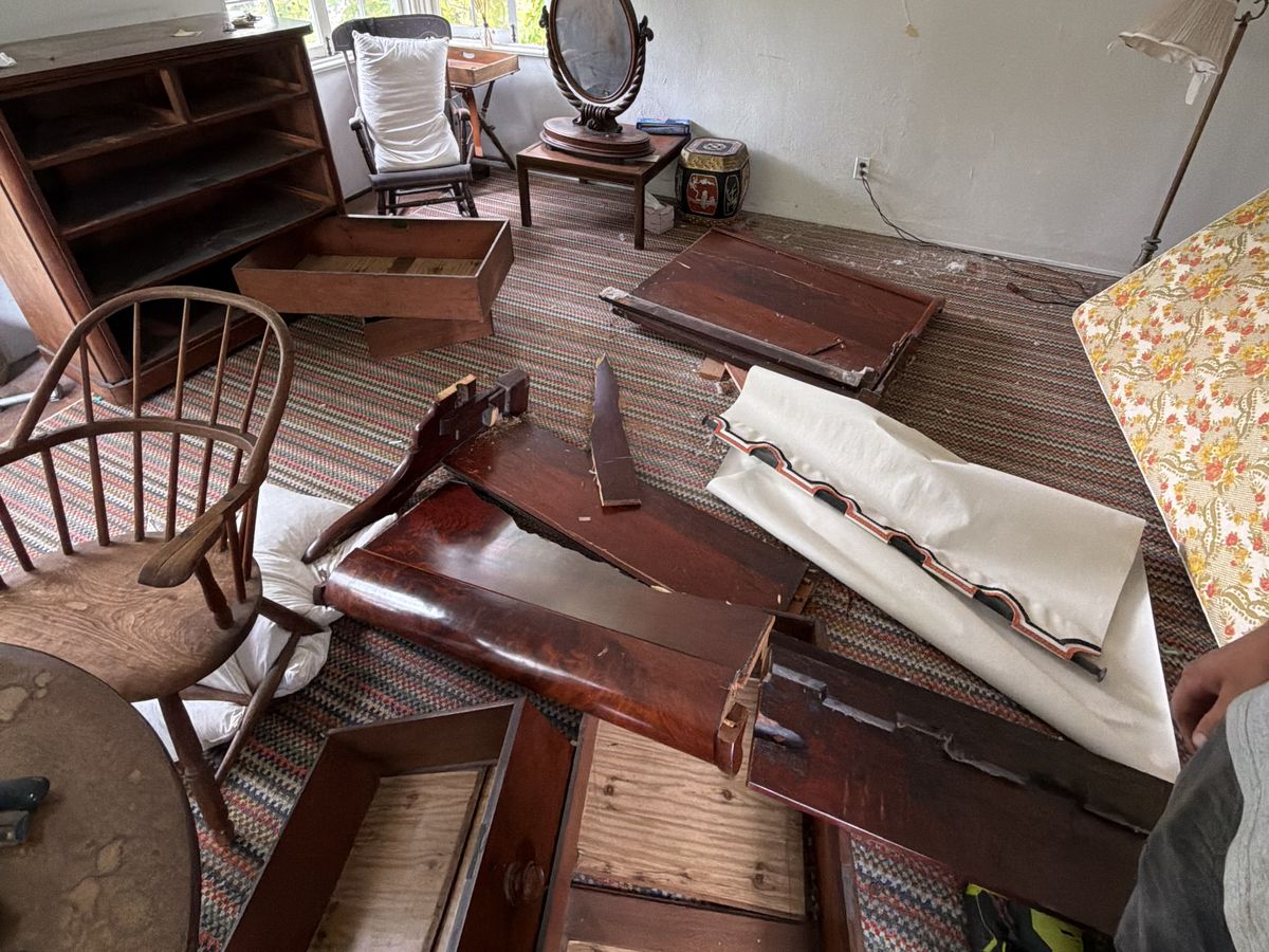 Room filled with broken antique furniture, drawers and boards across the rug, before