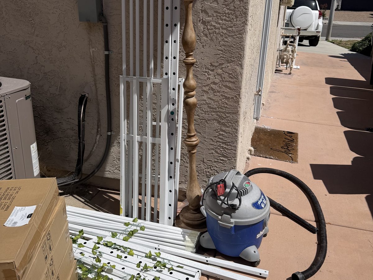 Side yard walkway blocked by old railings, a lamp, a shop vac and boxes, before