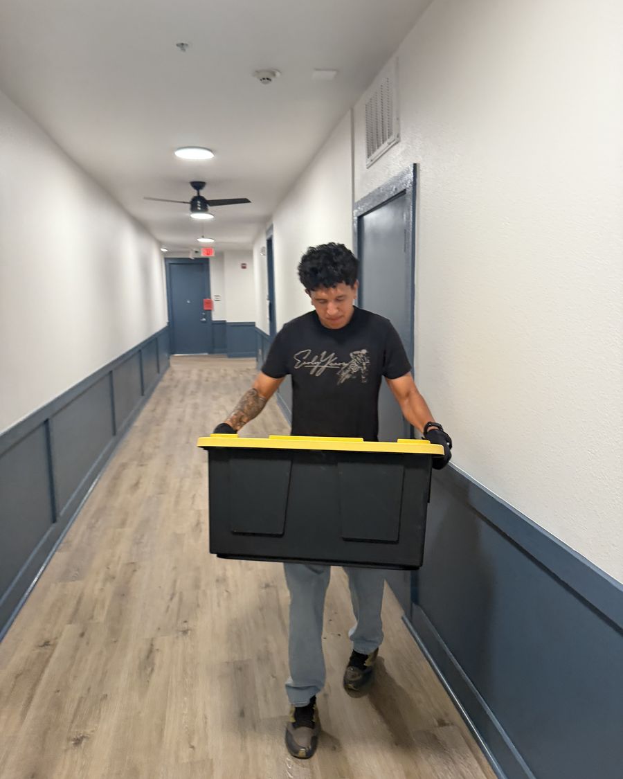 Crew member carrying a storage bin down an apartment hallway on a moving help job